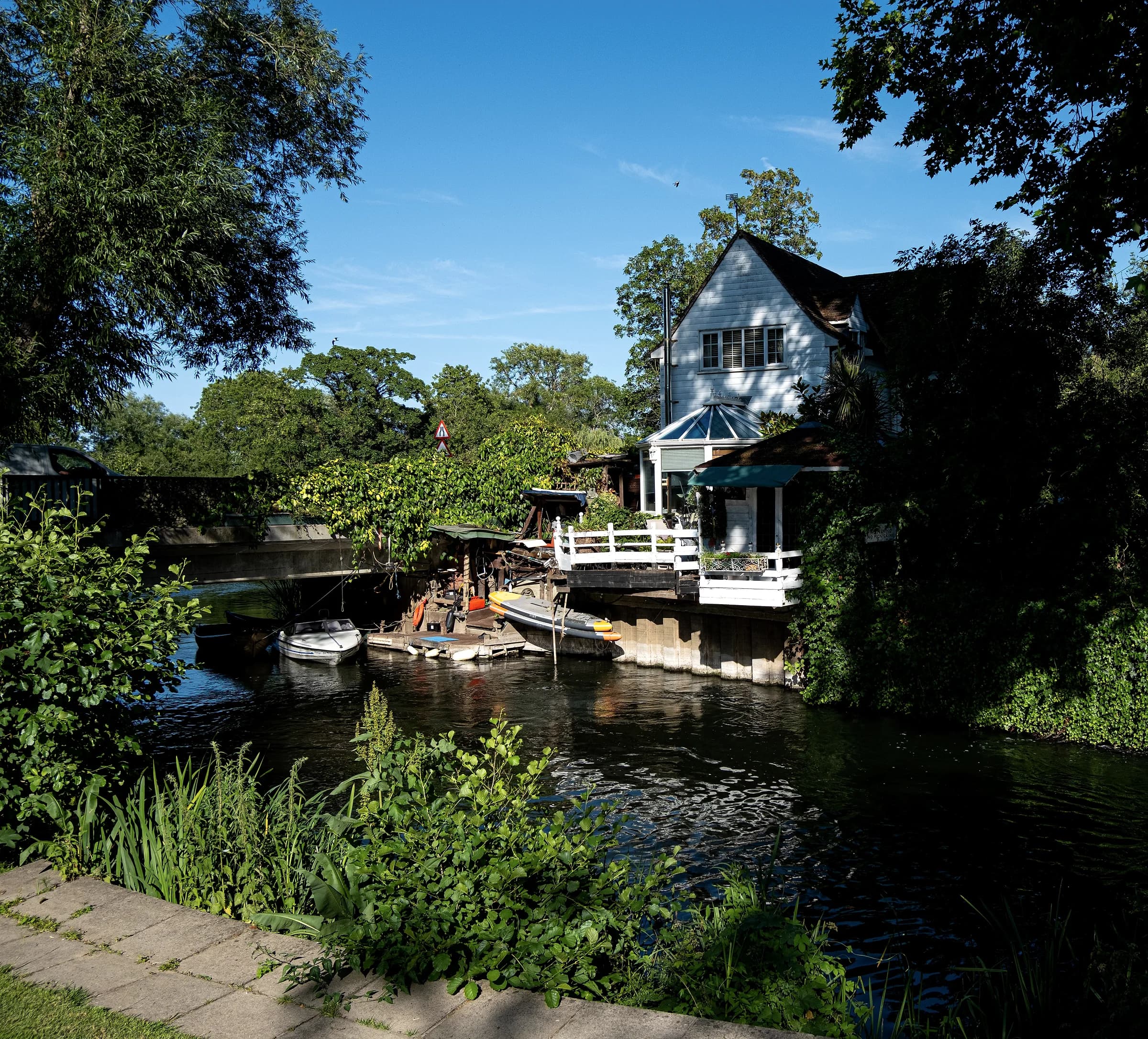 A weatherboarded house at the water's edge, with boats moored below.