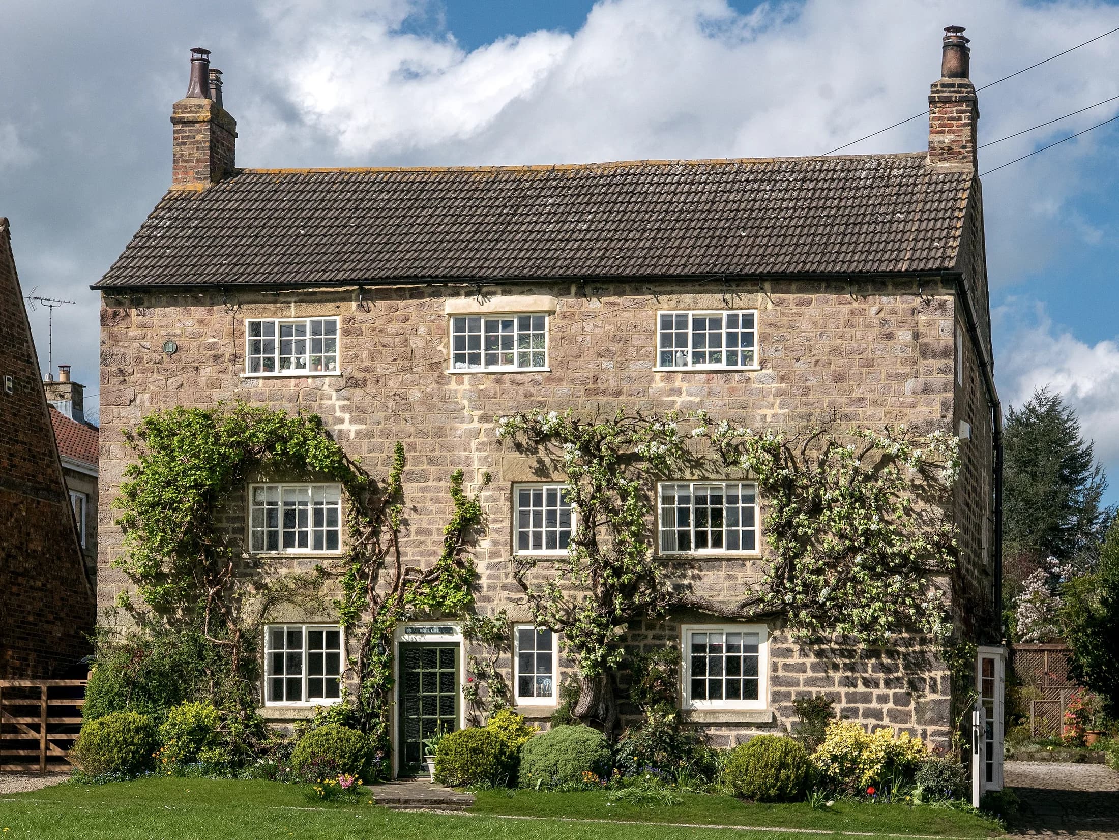 A stone-built English cottage with climbing wisteria across its facade.
