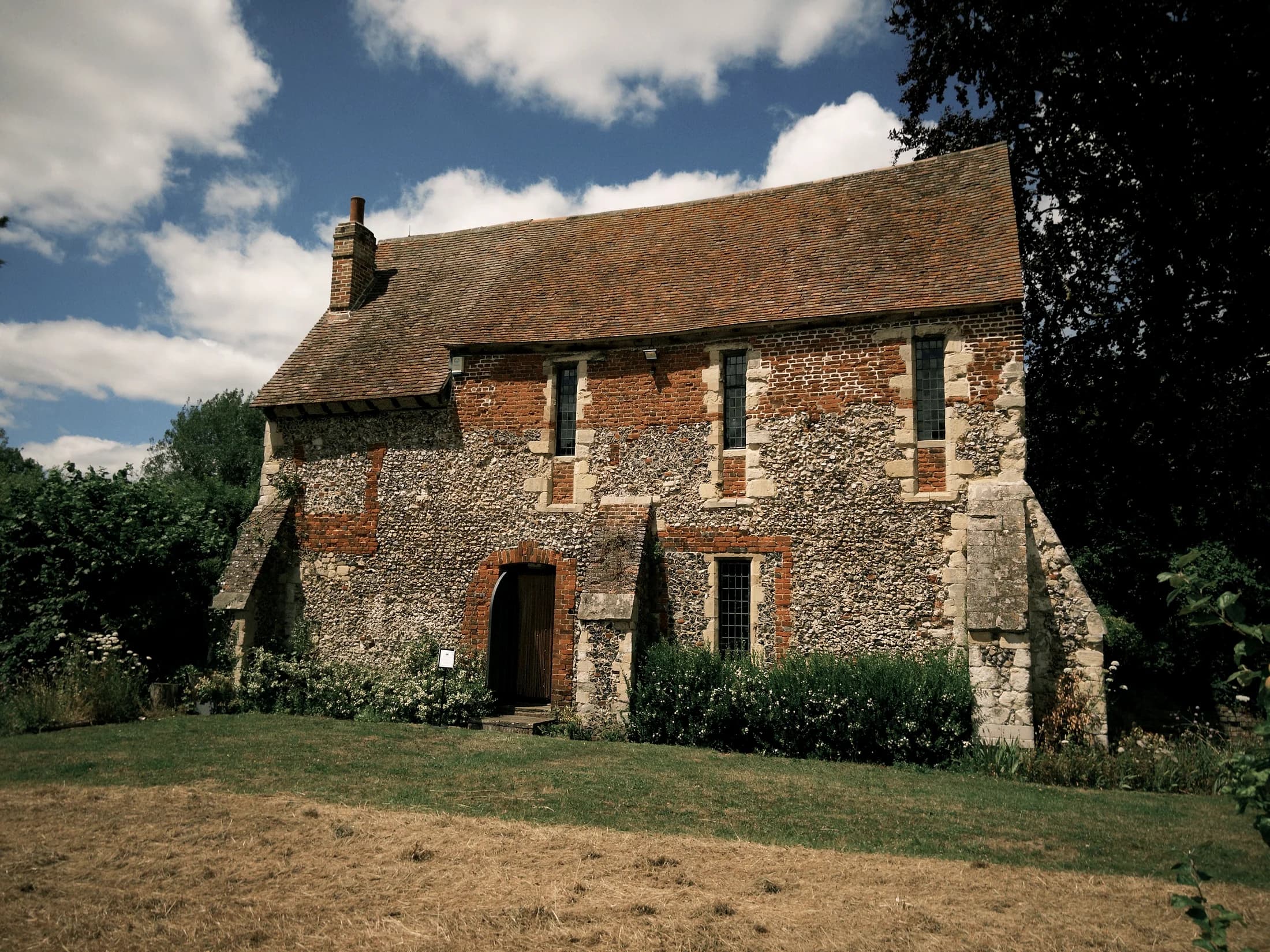 A flint and brick cottage under a wide summer sky.